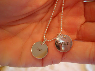 Hand holding necklace with two metal plates that say Om and Shanti