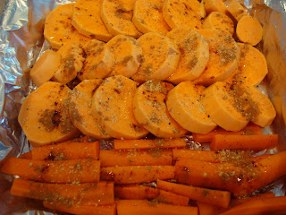 Sliced up sweet potato and carrot sticks in tinfoil lined pan toped with cinnamon and ginger
