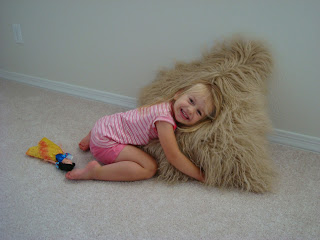 Young girl hugging large brown fuzzy pillow on floor