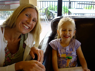 Woman crouching next to young girl sitting in chair smiling