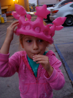 Young girl wearing pink blow up crown sucking on sucker