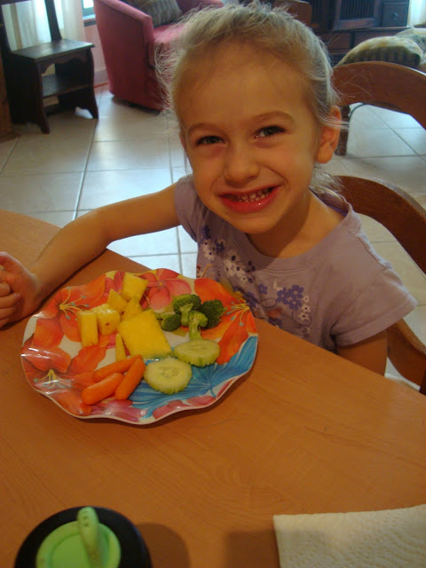 Young girl sitting eating plate of vegetables and fruit