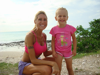 Woman squatting next to young girl on beach smiling