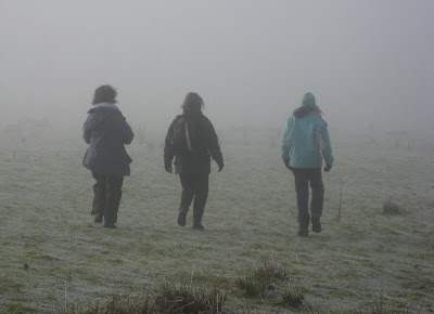 Three figures walking away into the mist on frosty ground