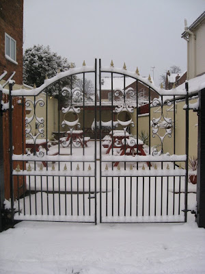 View of the snowy pub garden through the ironwork gates