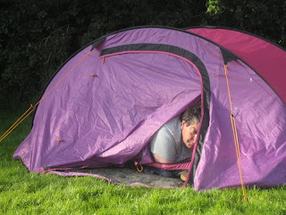 Groggy-looking man peering from the partly opened door of a bright pink tent