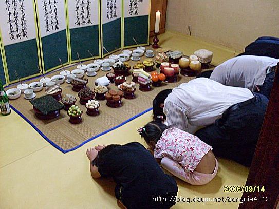 Familia coreana haciendo reverencia ante la ofrenda a sus antepasados