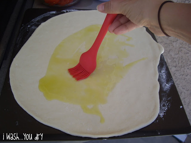 A pastry brush spreading olive oil onto rolled out pizza dough. 