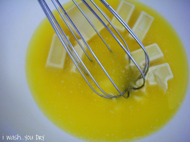 A wire whisk stirring milted butter and the squares of white baking chocolate. 