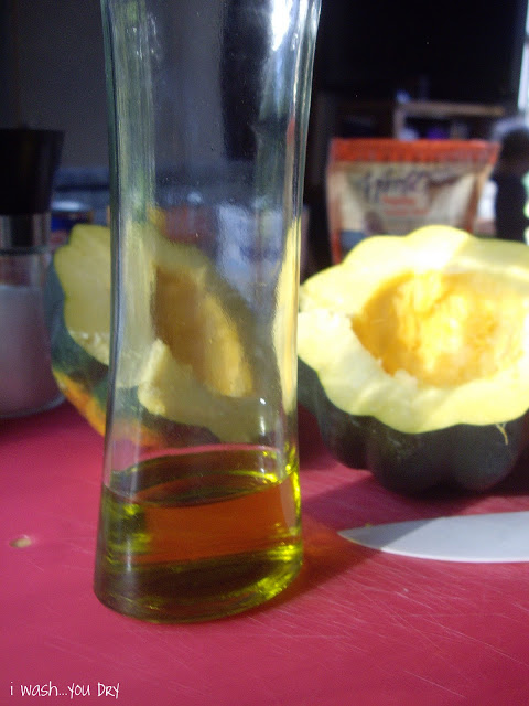 A bottle of olive oil next to a tow halves of a squash. 