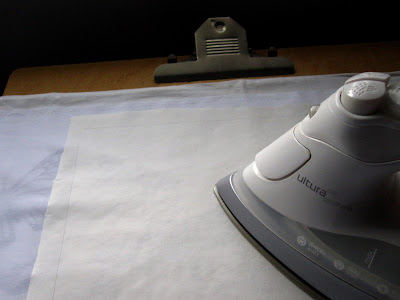 An iron pressing a piece of paper onto a length of white fabric.