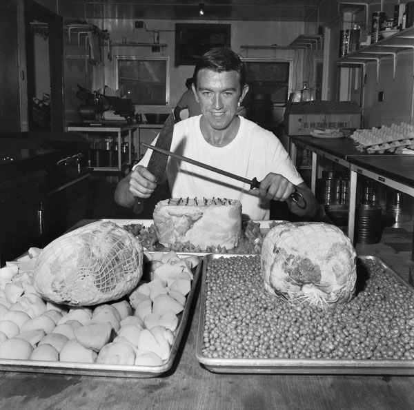 Nui Dat, South Vietnam. November 1970. Corporal Arthur Wallis, 21, of Preston, Vic, sharpening a knife in preparation for carving the three prime hams he has prepared for Christmas. He is one of 200 Army cooks who have been sharpening their wits, and their knives, to give Australian troops in Vietnam a slap-up Christmas lunch and dinner.