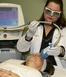 picture of dark haired woman wearing safety goggles administering fraxel to a woman lying on a gurney
