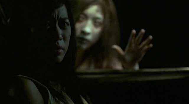 Uma moça tailandesa está dentro do que parece ser um carro olhando para o lado (de dentro) e um fantasma de mulher está com o rosto próximo ao vidro da janela olhando para a moça.