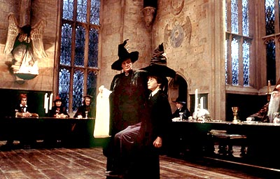 Harry Potter está sentado em um banco em um grande salão de janelas enormes em vitral. A professora McGonagall coloca sobre a cabeça dele o chapéu seletor. Ao fundo, uma longa mesa é ocupada pelos professores bruxos.