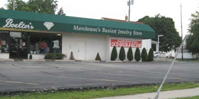 Empty parking lot and boxy store with green awning that reads Manitowoc's Busiest Jewelry Store