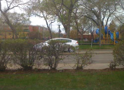 Silver Prius driving past a playground and green grass