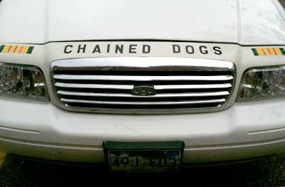 Front end of a white full-sized Ford with the words CHAINED DOGS above the grill
