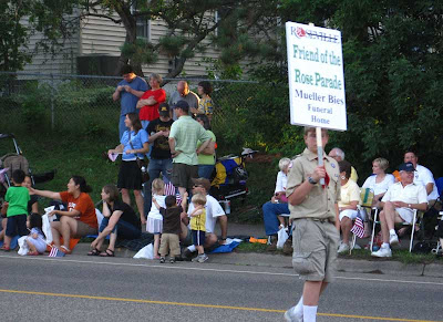 Boy Scout carrying a sign on a stick, reading Rose Parade sponsor Mueller Bies Funeral Home