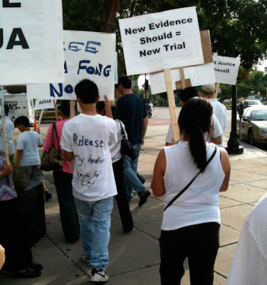 Backs of demonstrators with signs. One man's hand-written shirt says Release My Brother Koua Fong Lee