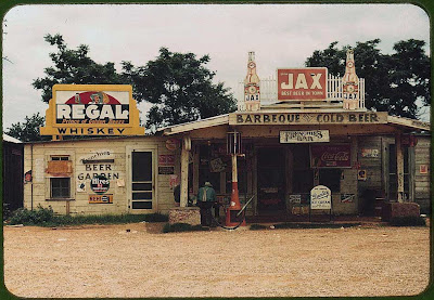 Two weathered buildings covered with signs for beer, barbeque and more