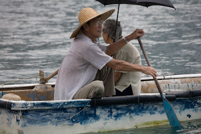 Old man and wife in a rowboat with umbrella