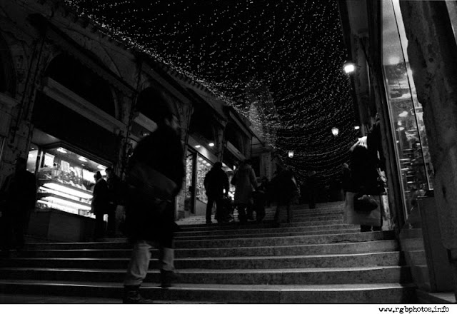Fotografia notturna in bianco e nero a Venezia: un passante cammina per una calle addobbata a festa