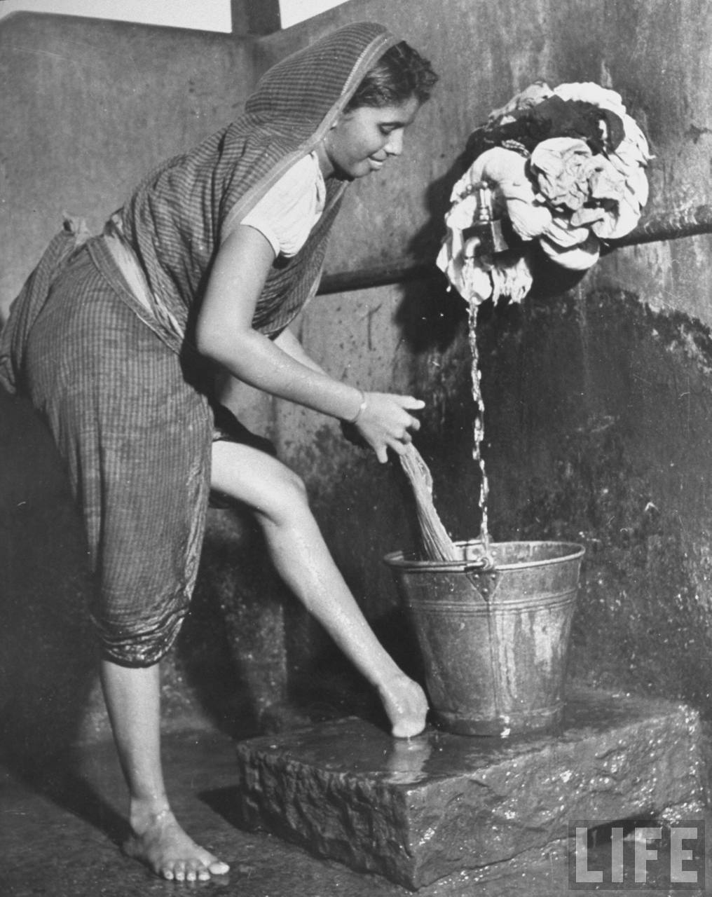 Young Indian woman washing clothes at the public water stand in the