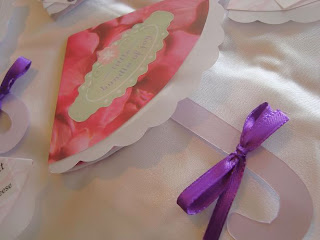 Layed out umbrella-shaped invitation with rose-patterned hood, cardstock umbrella handle, and purple ribbon