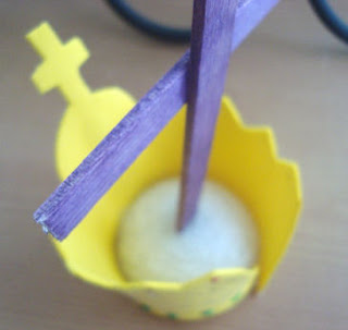 Styrofoam half-sphere with yellow foam crown around it and purple cross in it