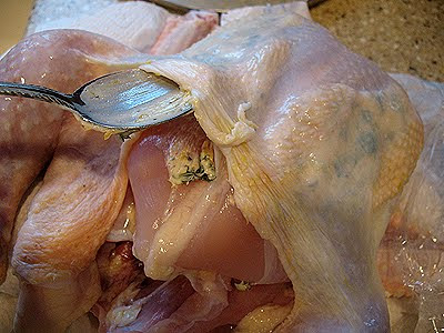 A close up photo of the butter mixture being placed under the skin of the chicken.