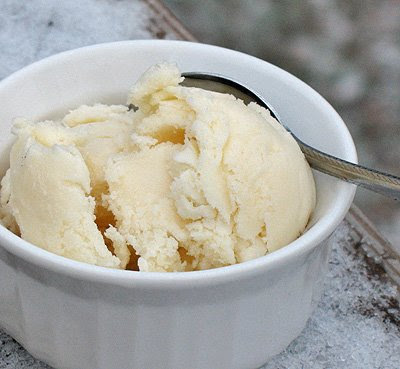 A close up photo of a scoop of homemade vanilla ice cream in a white bowl served with a spoon.