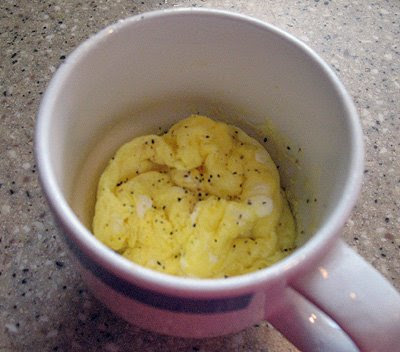 A close up overhead photo of scrambled eggs in a mug with pepper on top.