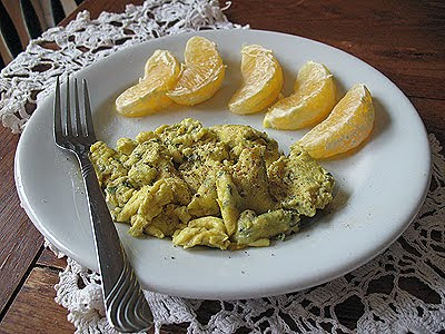 A photo of scrambled eggs with garlic, basil and feta resting on a plate with orange wedges to the side.