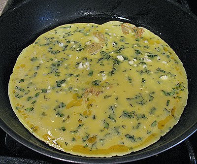 A photo of eggs with garlic, basil and feta cooking in a skillet.