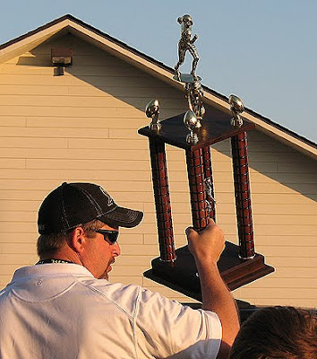 A photo of the football coach holding the division championship trophy.