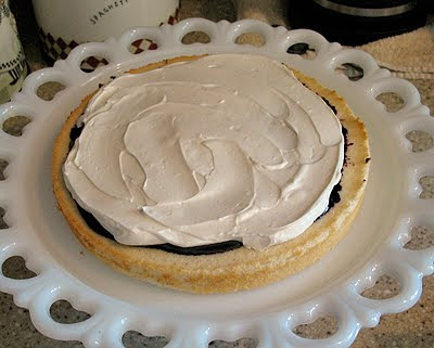 A photo of the first layer of a vanilla bean mulberry cake resting on a cake stand with syrup and frosting layer on top. 