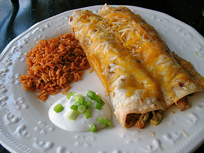 Shredded chicken and Chile enchiladas on a white plate with Spanish rice and sour cream on the side.