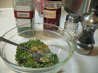 A bowl of garlic seasoning, chopped chives, salt and pepper.