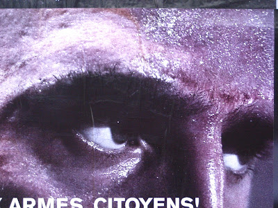 photo of a billbord displaying a pair of grim darj eyes and the words Armes Citoyens partially visible at the bottom