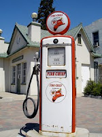 Photo of an old gas pump in front of a steep-roofed building.