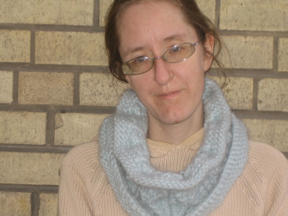 A woman wearing a bulky-weight blue cowl loose around her neck. 